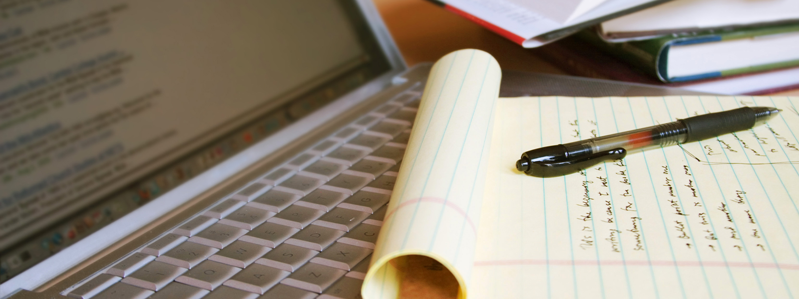 Laptop computer with books, pen and yellow legal pad.