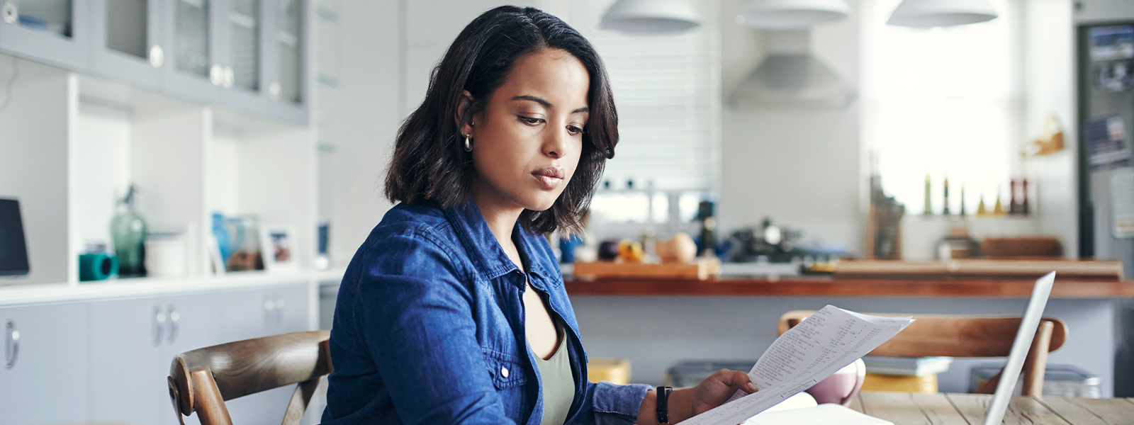 A young woman using a laptop and going through paperwork while working from home.