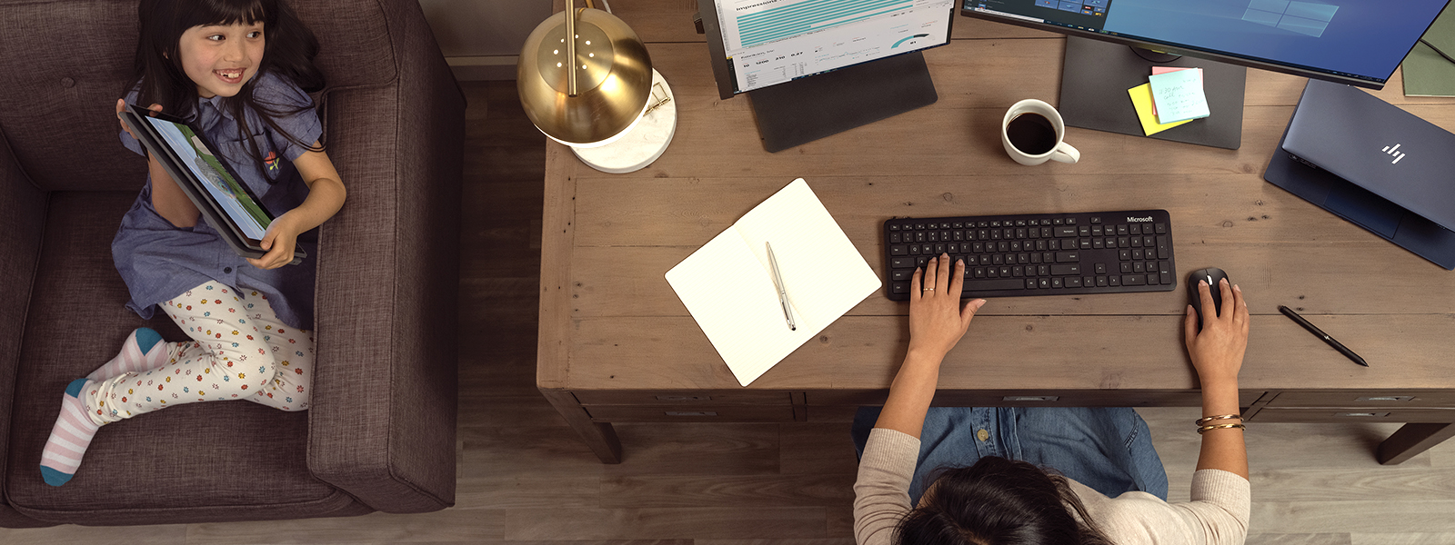 a mother working from home while talking to her little daughter playing on a tablet.