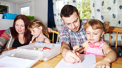 the Kenney family of four coloring together on paper at the kitchen table