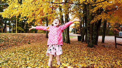 a girl playing outside in the fall colored leaves