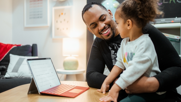 A Father and Daughter Smiling at Each Other Using a Microsoft Surface Tablet on a Table