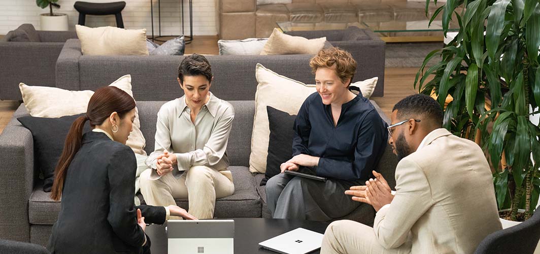A small group of people on couches and chairs gathered around a laptop.