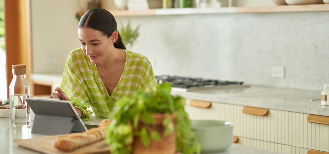 A woman using a tablet on the kitchen island to plan Mother’s Day dinner.