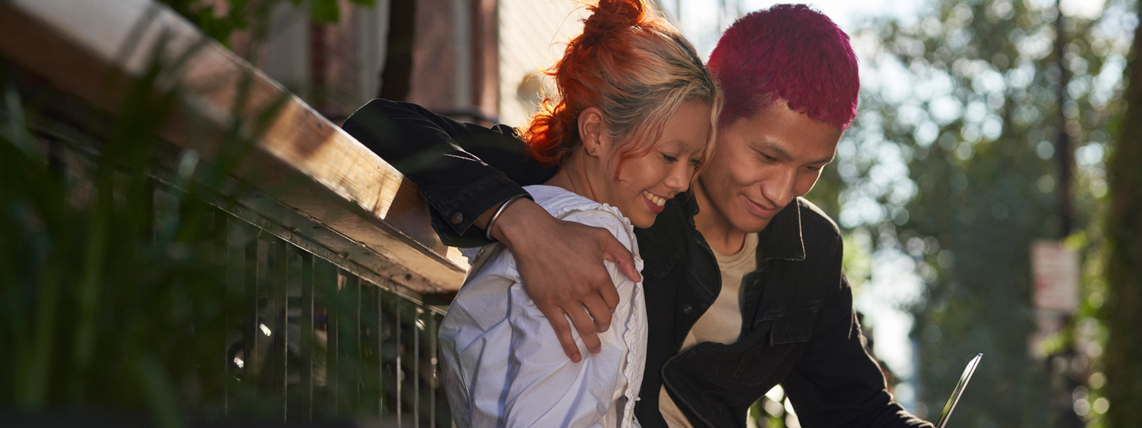 A young couple leaning against a railing looking at a tablet together.