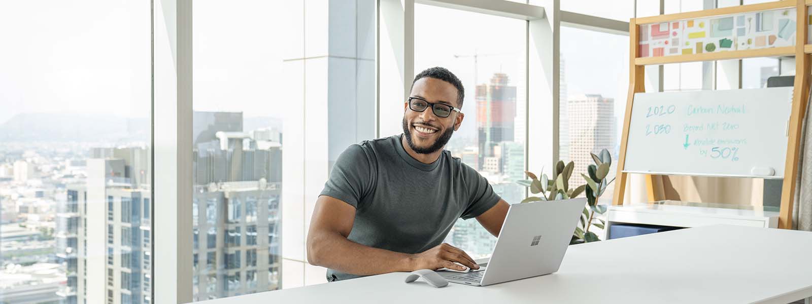 A man smiling in front of a laptop sitting in a meeting room in a skyscraper.