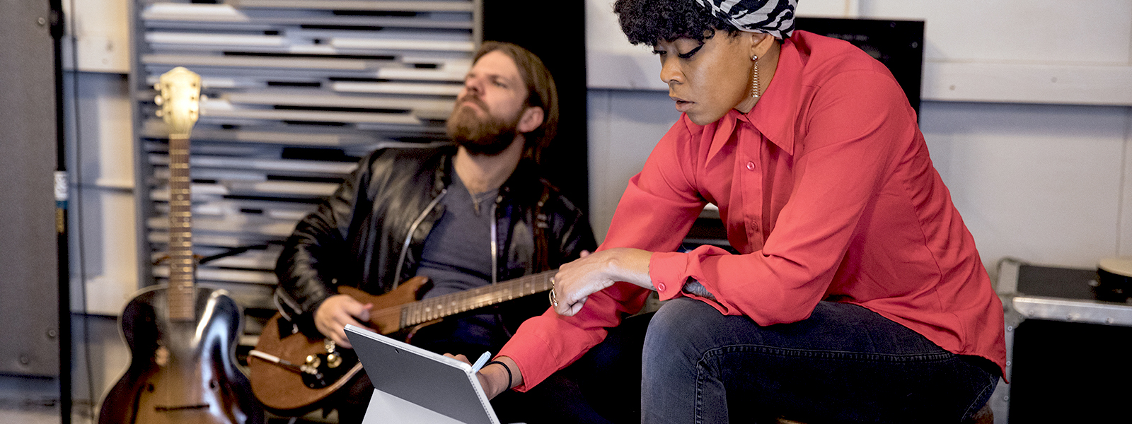 Man playing guitar while woman takes notes on tablet in a music studio.