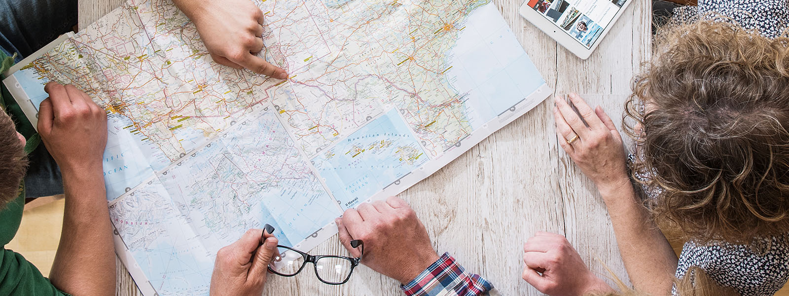 a family of four people gathered around a map and a person pointing to a location on the map.