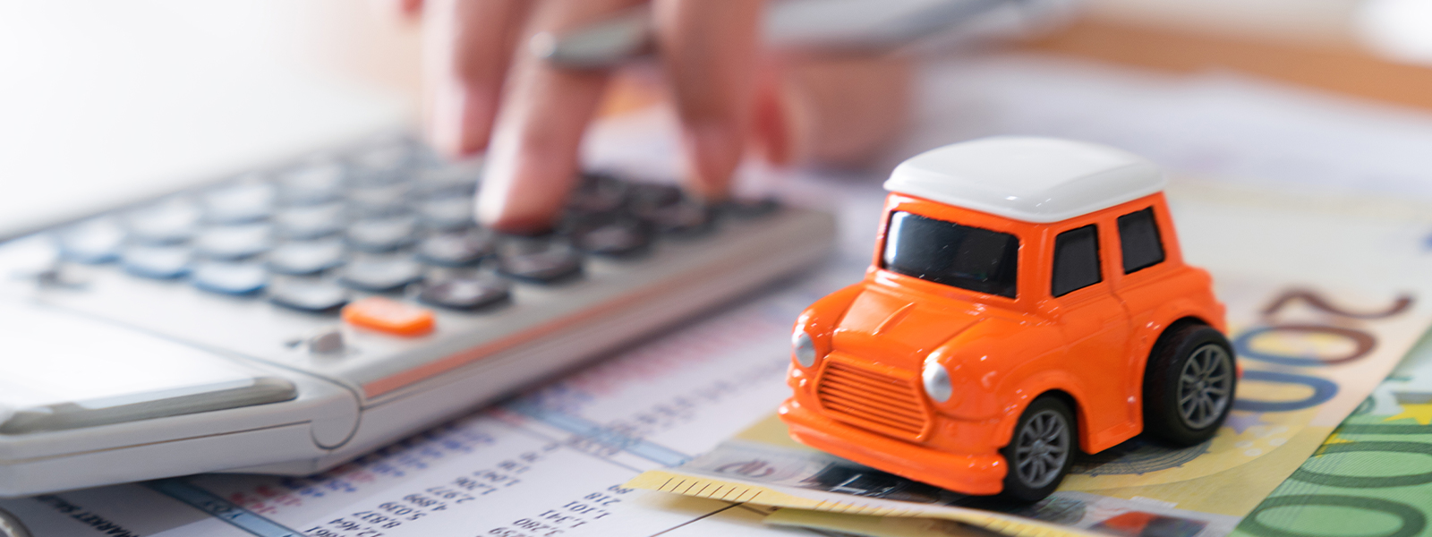 A person calculating costs to buy a car with flat lay of miniature car model, calculator and pen on office desk table.