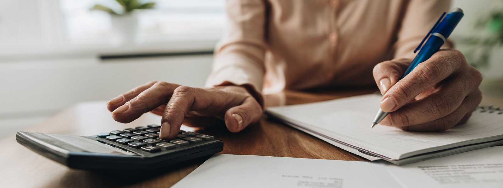 Close up of unrecognizable woman using calculator while going through bills and home finances.