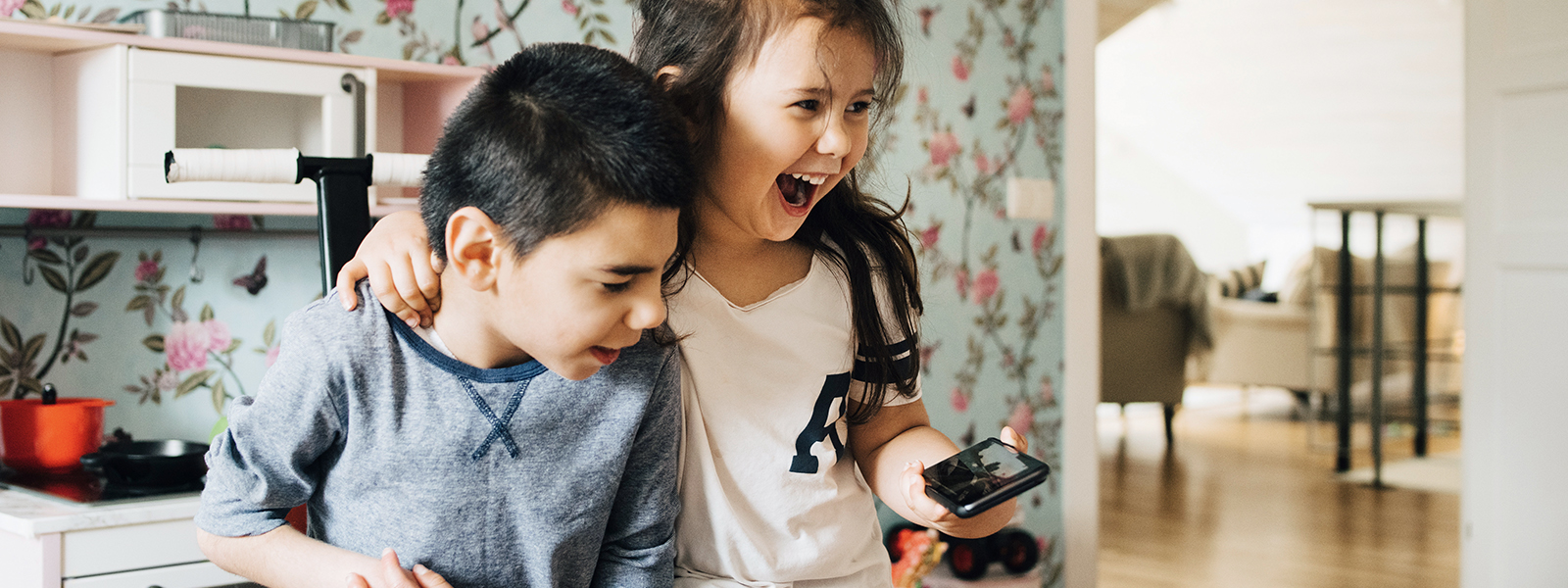 two kids laughing while using a phone.