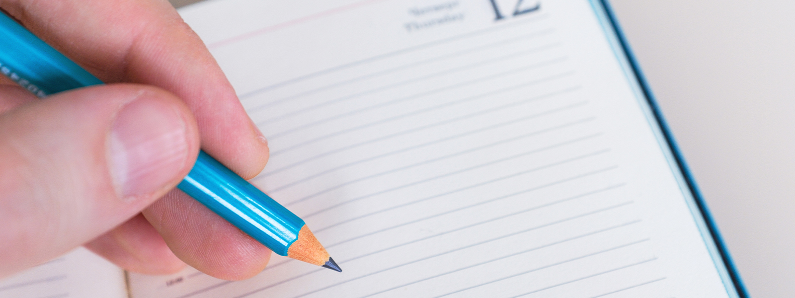 A hand with pencil writing on white notebook.