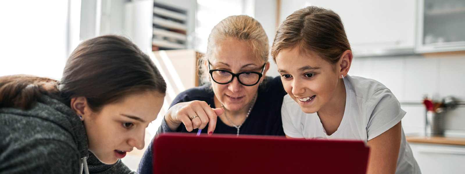 Mother helping her daughters to finish school homework during coronavirus quarantine. They are using a laptop. 