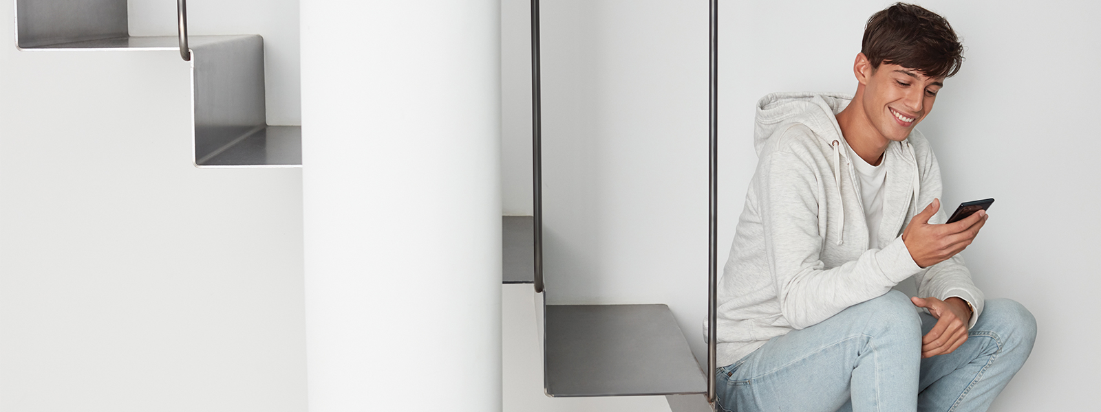 a male student inside home, smiling, and looking at his phone. 