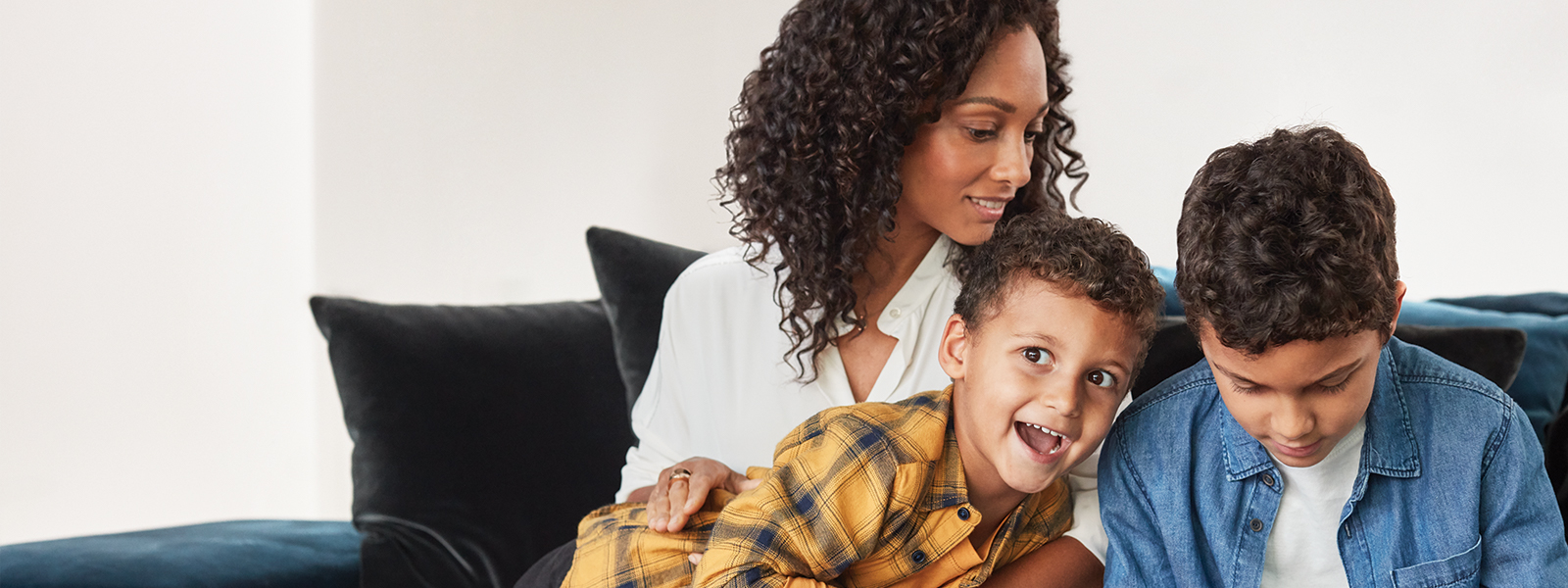 Mother and sons inside home hanging out with child playing games on Surface Go. 