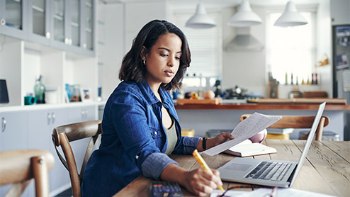 a young woman using a laptop and going through paperwork while working from home