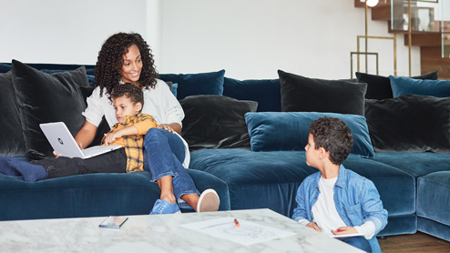 Mother and sons inside home hanging out while using laptop.