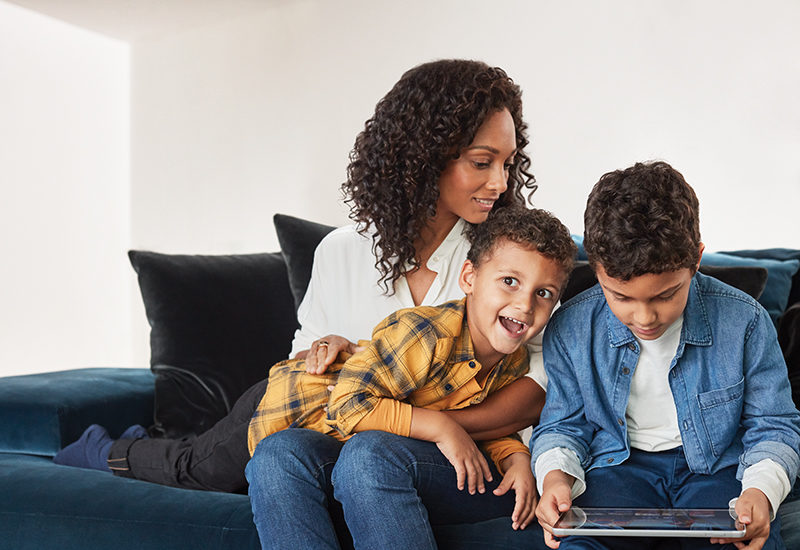 Mother and sons inside home hanging out with child playing games on Surface Go.