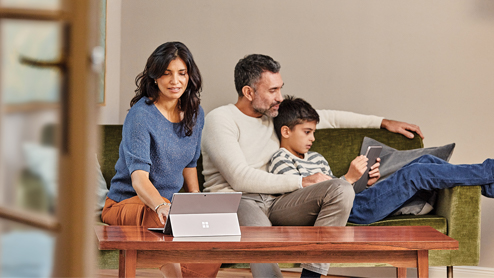 Family at home in sofa with mobile professional mother on Surface Pro, father and son on Surface Go.