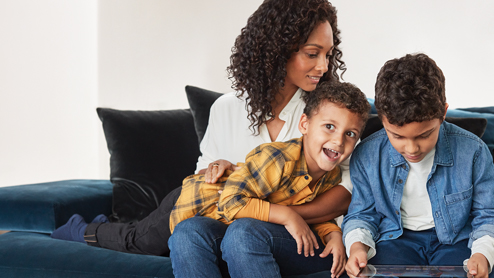 Mother and sons inside home hanging out with child playing games on Surface Go.