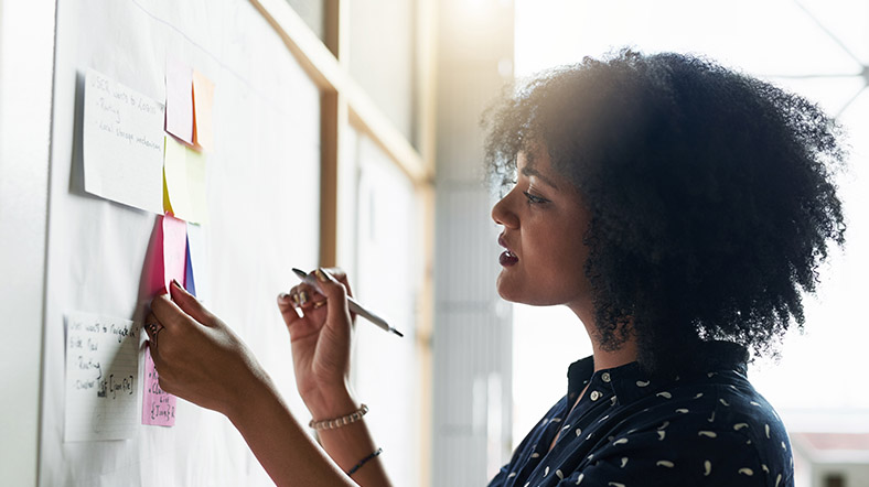 a young female designer working in her office looking at diferent colored sticky notes on a board