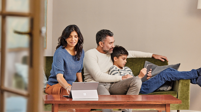 Family at home in sofa with mobile professional mother on Surface Pro, father and son on Surface Go.