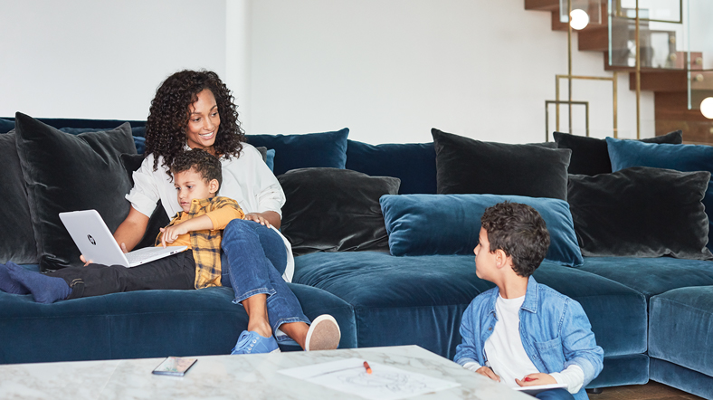 Mother and sons inside home hanging out while using laptop.